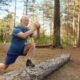 Handsome energetic senior man with beard wearing sports clothes doing cardio routine in wild nature. Elderly man having joyful confident look keeping foot on log, training leg muscles before run