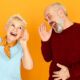 Body language. Portrait of two funny elderly Caucasian pensioners with hearing problem having conversation, keeping hands at ear and shouting but can not make out any words. Deafness concept